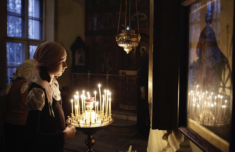 Девушка со свечой перед иконой в храме.